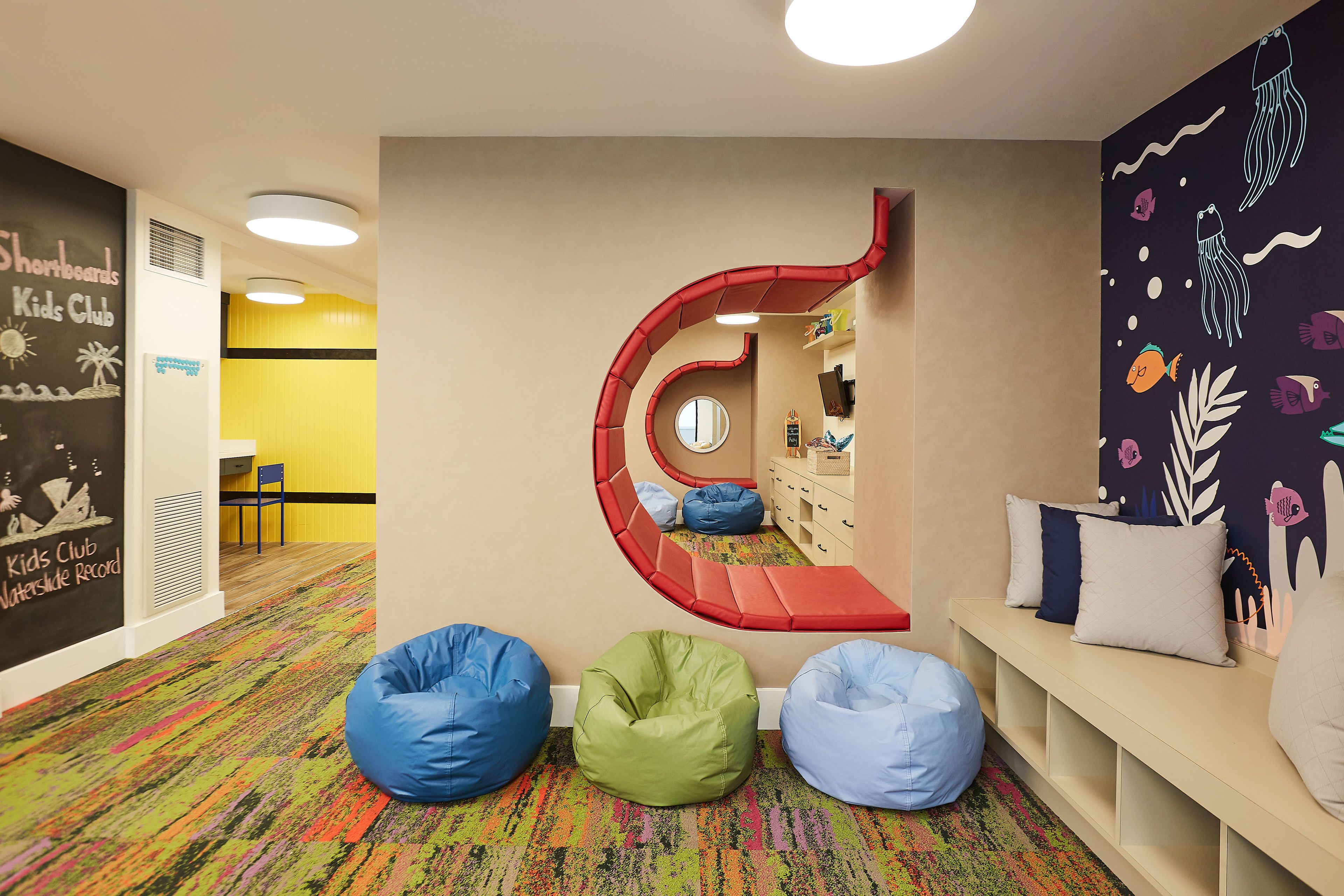 A children's play area with colorful bean bags, a spiral slide, and a wall mural.