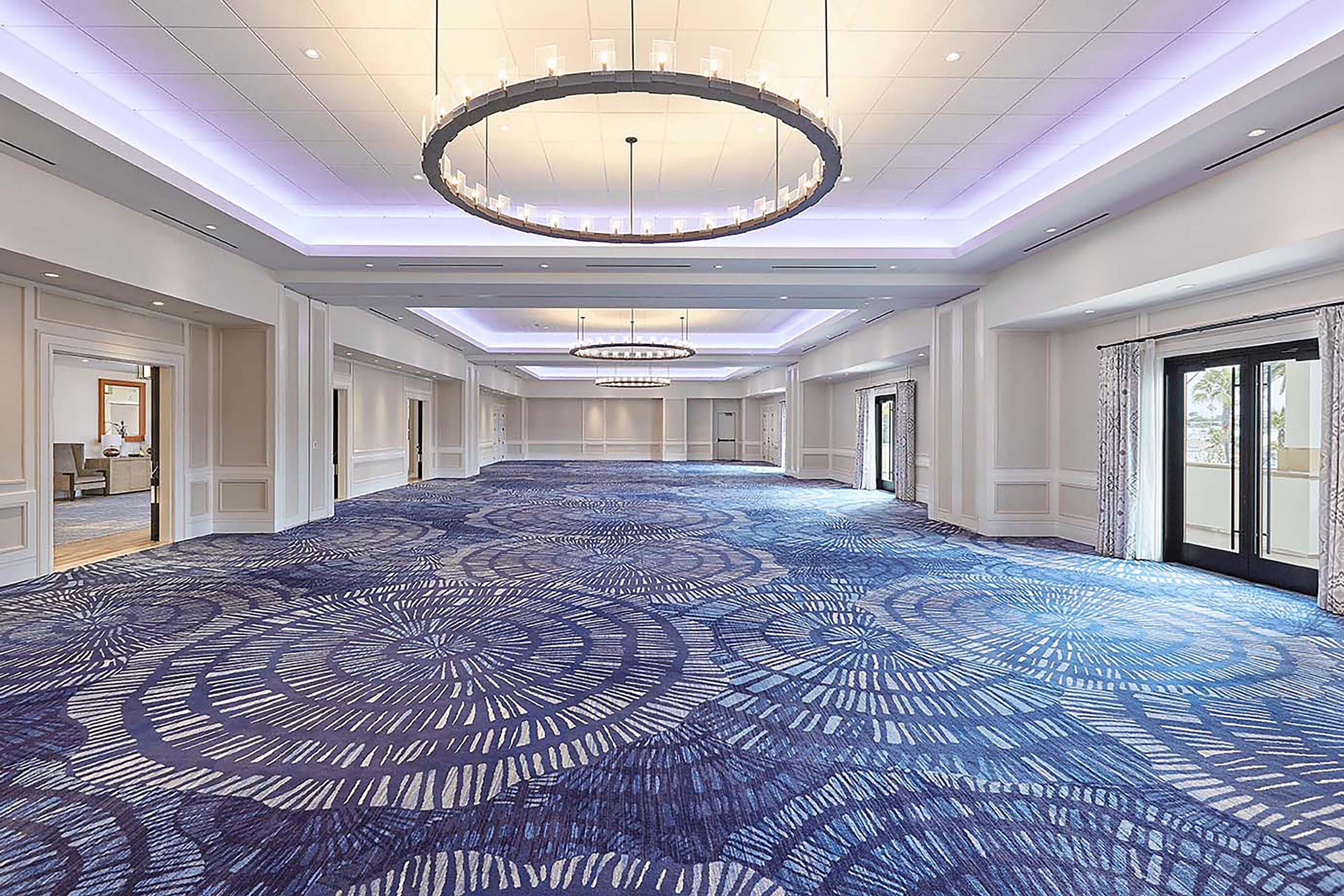 A long hallway with a patterned carpet, large circular chandeliers, and doors on both sides.