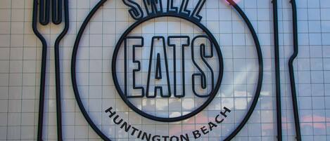 A sign with the words "SWELL EATS" and "HUNTINGTON BEACH" on a tiled wall.