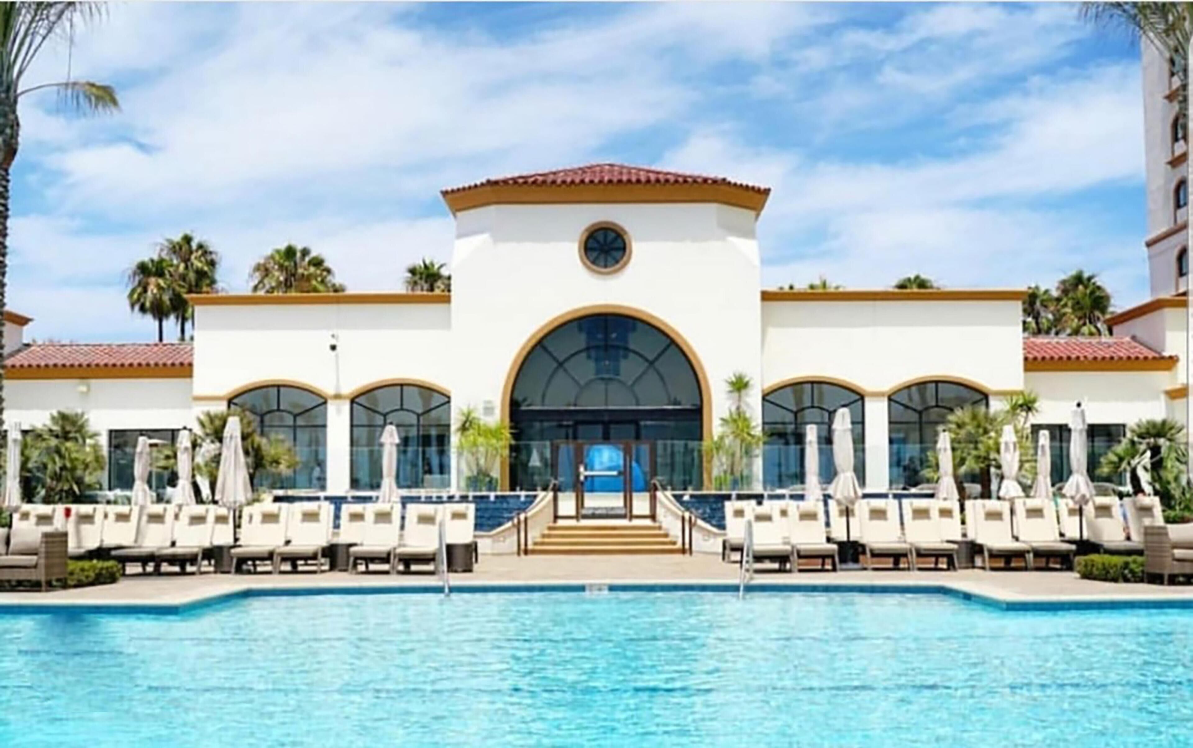 A hotel with a pool, lounge chairs, and palm trees.
