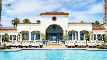 A hotel with a pool, lounge chairs, and palm trees.