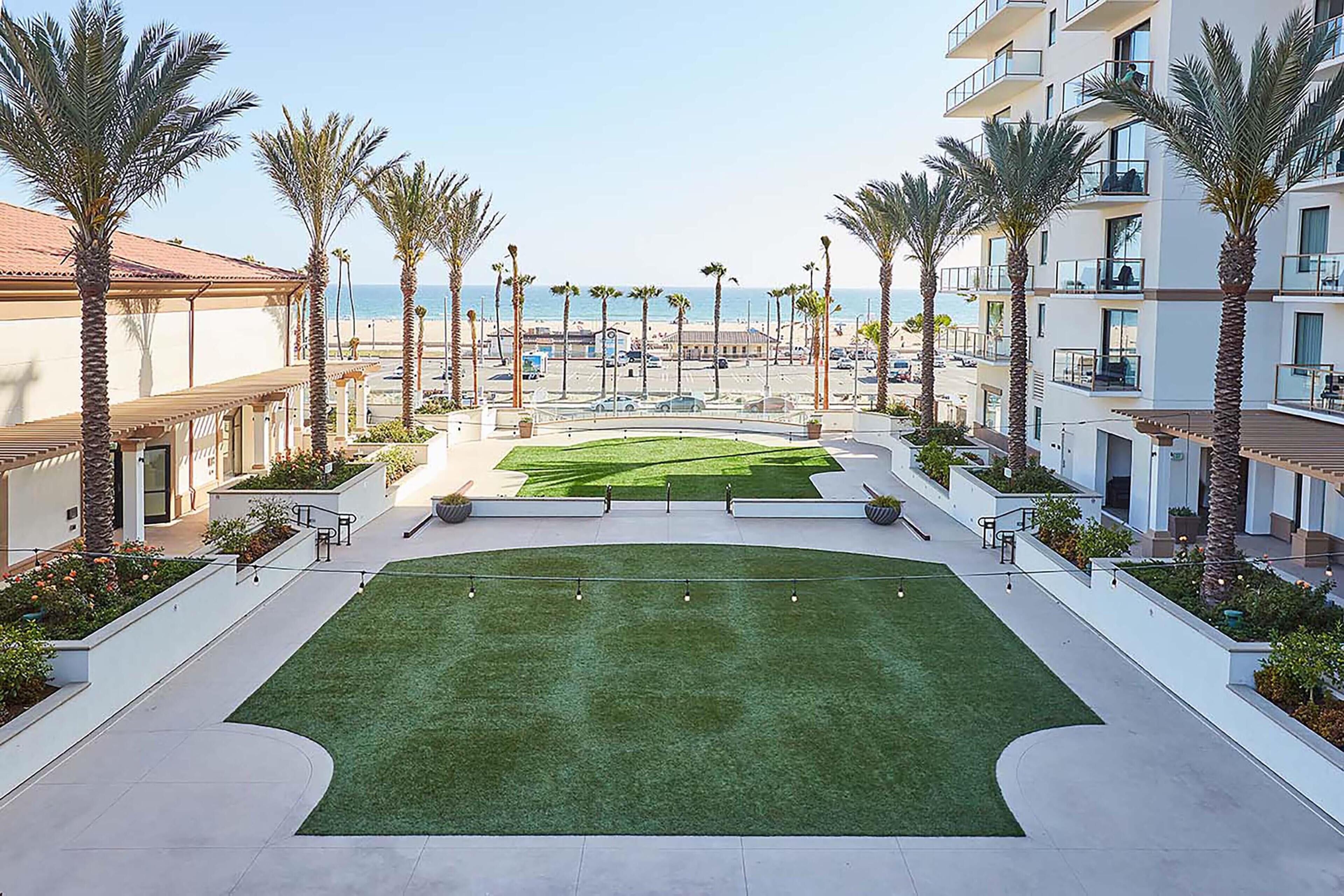 A courtyard with a green lawn, palm trees, and a view of the sea.