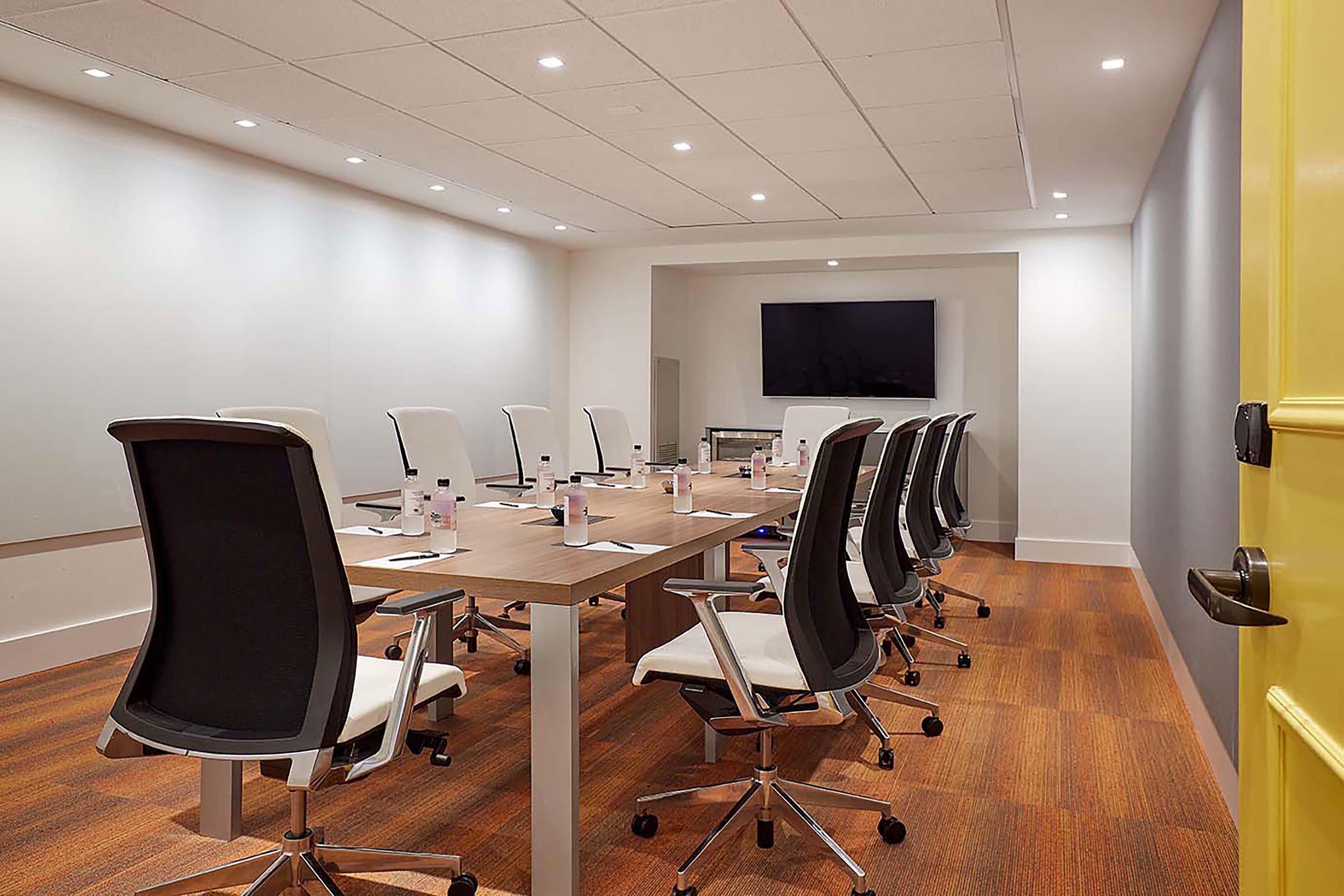 A conference room with a long table, multiple chairs, a flat-screen TV, and a yellow door.