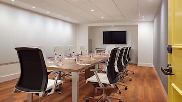 A conference room with a long table, multiple chairs, a flat-screen TV, and a yellow door.