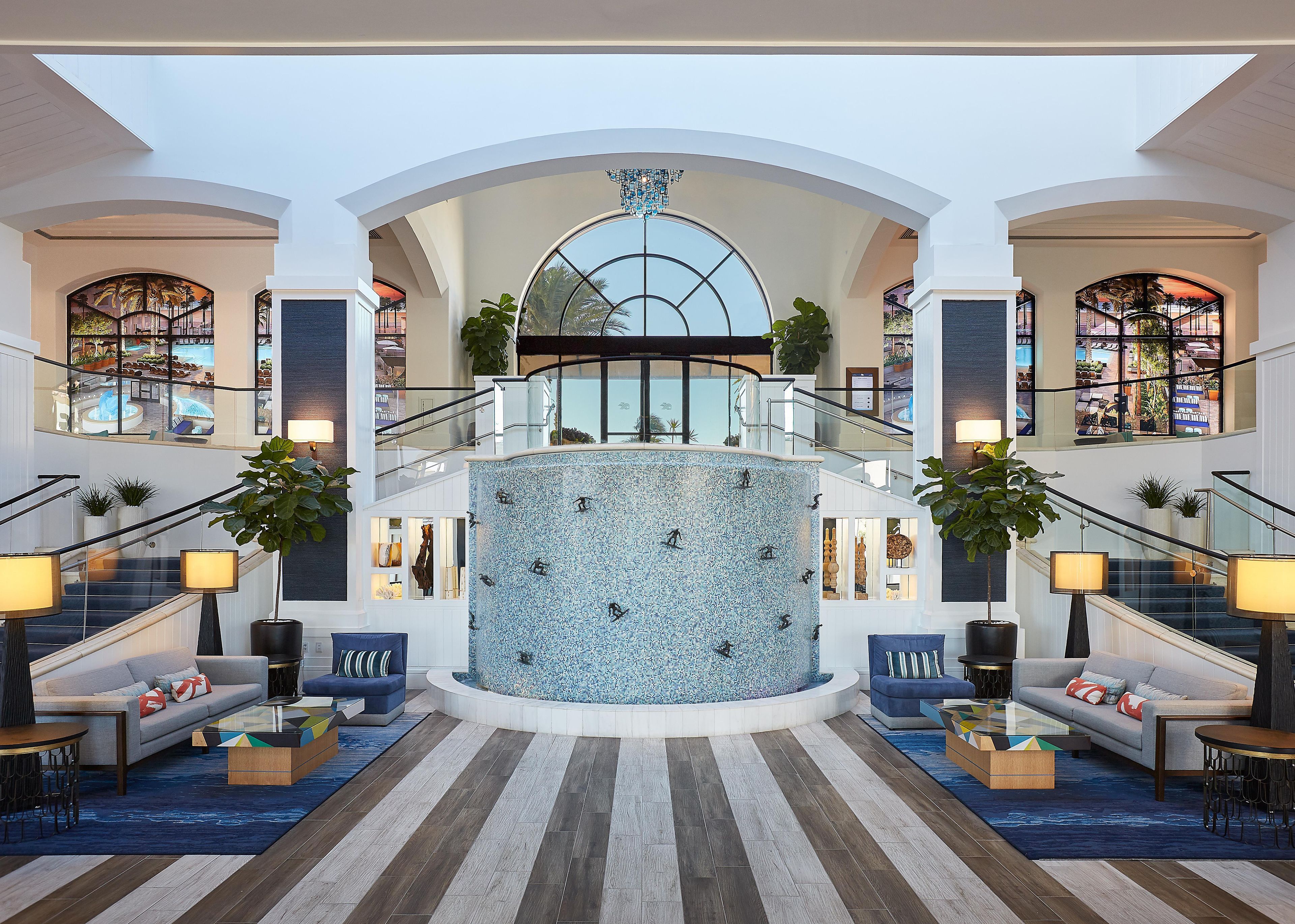 Een ruime lobby met een centrale fontein, diverse zithoeken en uitzicht op het zwembad.