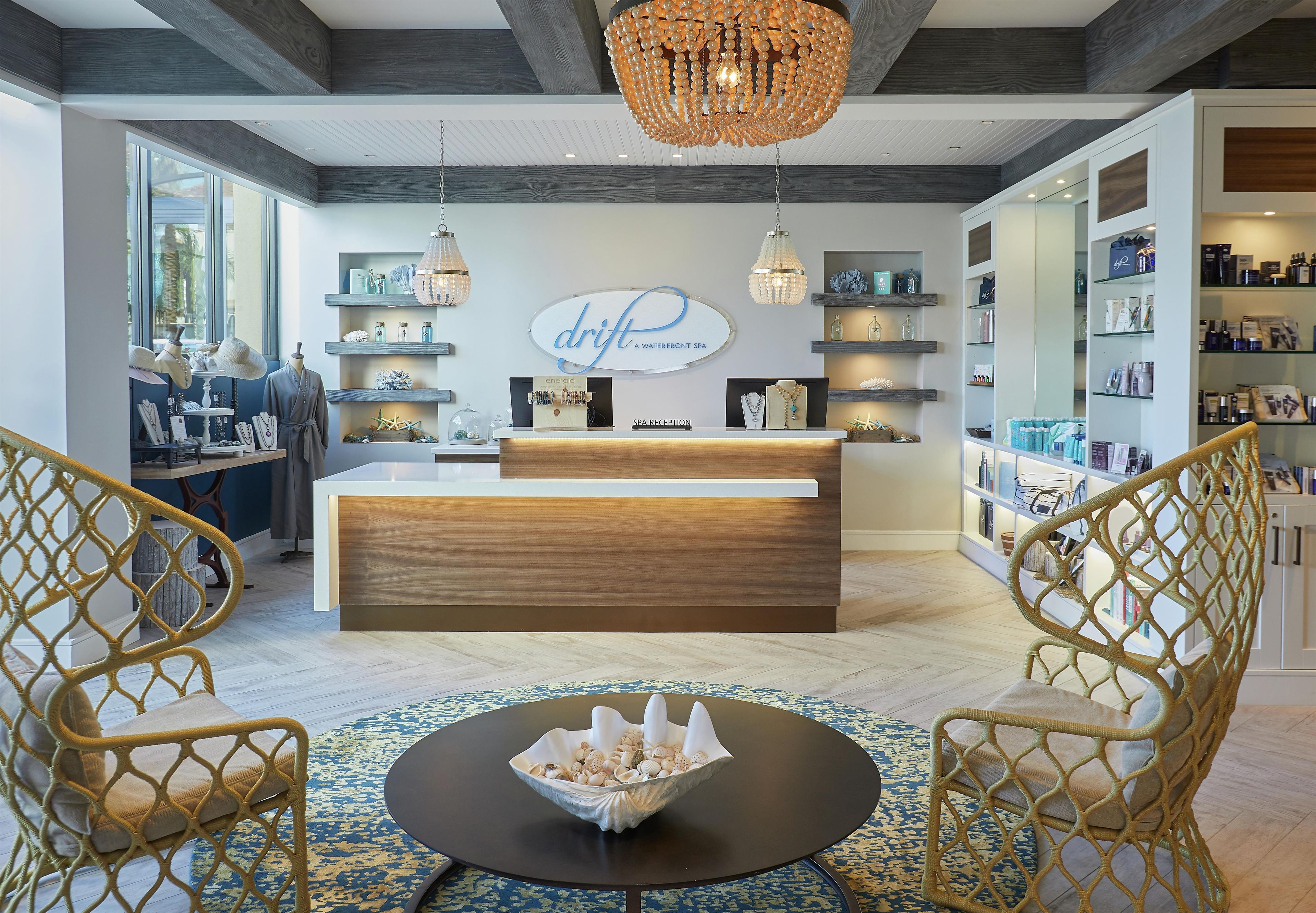 Un espace d’accueil avec un comptoir de réception en bois, un lustre, des fauteuils en osier et un vase décoratif posé sur une table ronde.
