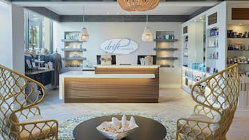 Un espace d’accueil avec un comptoir de réception en bois, un lustre, des fauteuils en osier et un vase décoratif posé sur une table ronde.