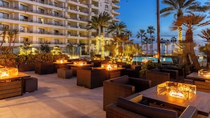 A hotel with outdoor seating areas, palm trees, and a pool. - The Waterfront Beach Resort, A Hilton Hotel (Huntington Beach)
