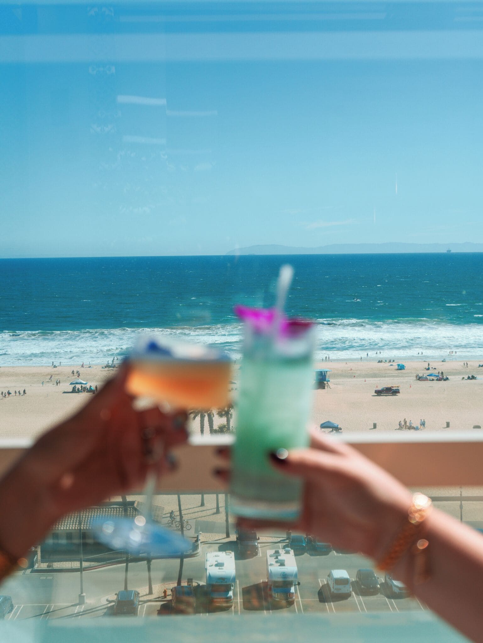 Vue sur la plage depuis un balcon doté d’une balustrade en verre, avec vue sur l’océan et un parking.