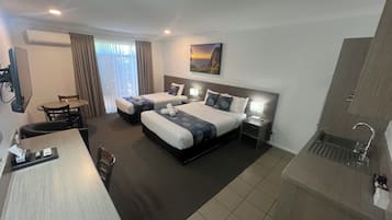Een hotelkamer met twee bedden, een bureau, een stoel, een kleine tafel, een televisie, een schilderij aan de muur en een wastafel.