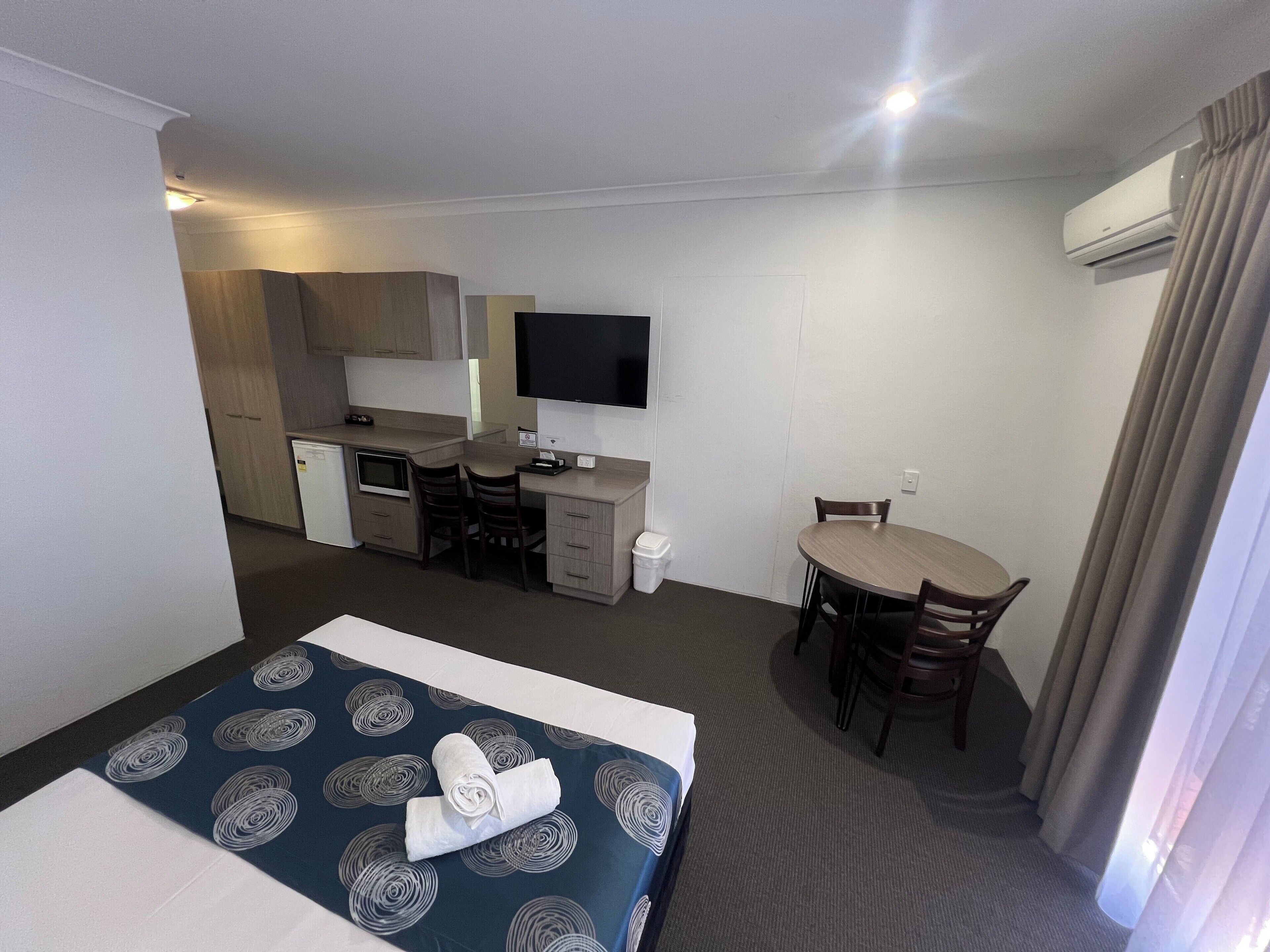 Una habitación de hotel con cama, escritorio, silla, kitchenette pequeño y televisión.