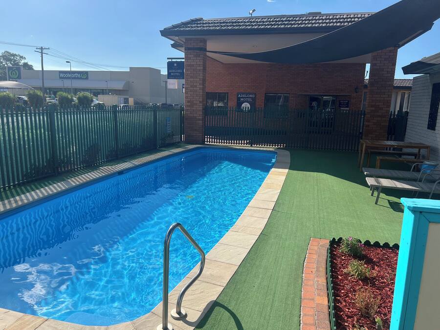 A swimming pool with a metal ladder, surrounded by a fenced area with a brick building in the background.