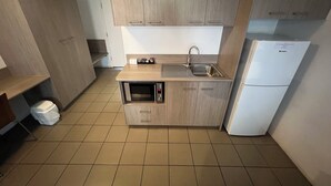 Une cuisine compacte avec des meubles en bois, un four à micro-ondes encastré, un évier et un réfrigérateur blanc.