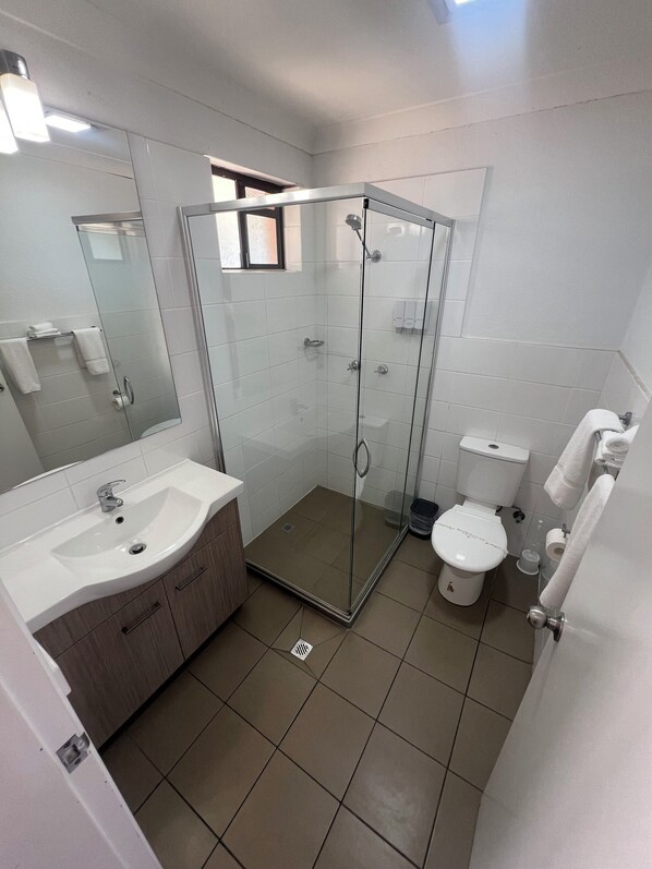 Un baño moderno con ducha acristalada, lavabo blanco y retrete.