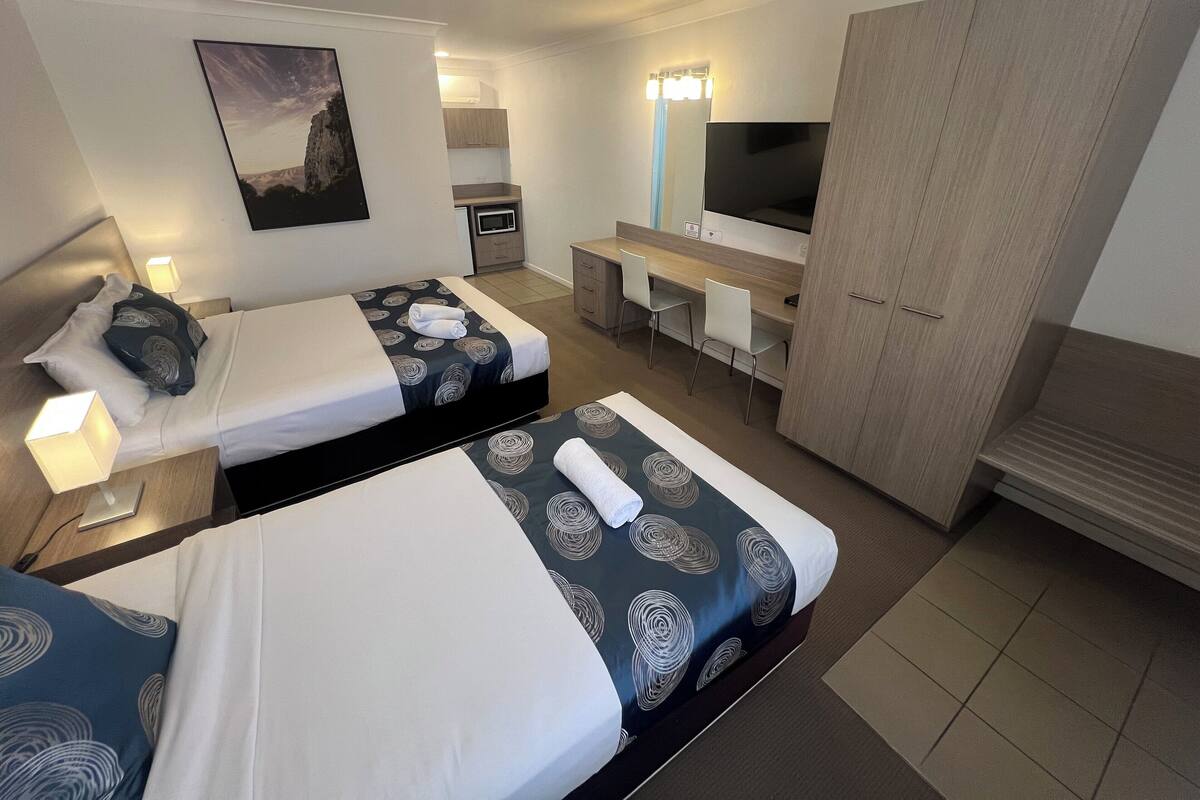A hotel room with two beds, a desk, a TV, and a wardrobe.