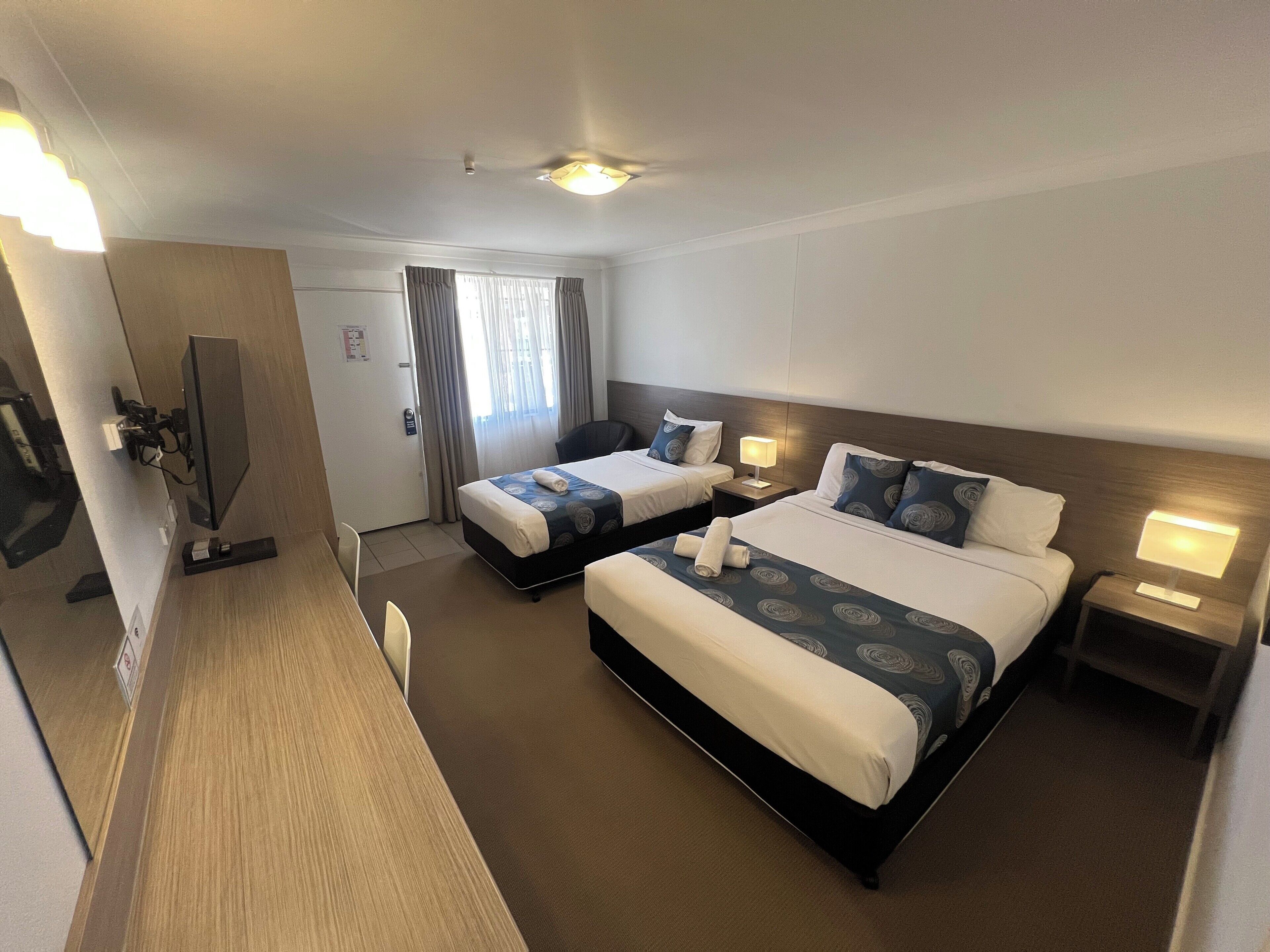 A hotel room with two beds, a desk, a chair, a TV, and a window with curtains.