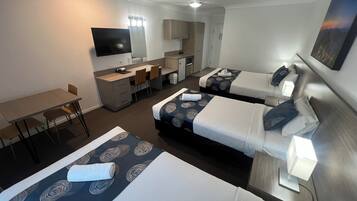 Ein Hotelzimmer mit zwei Betten, einem Schreibtisch, einem Stuhl, einem Fernseher und einer kleinen Küchenzeile.
