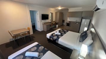 Een hotelkamer met twee bedden, een bureau, een stoel, een televisie, een kitchenette en een badkamer.