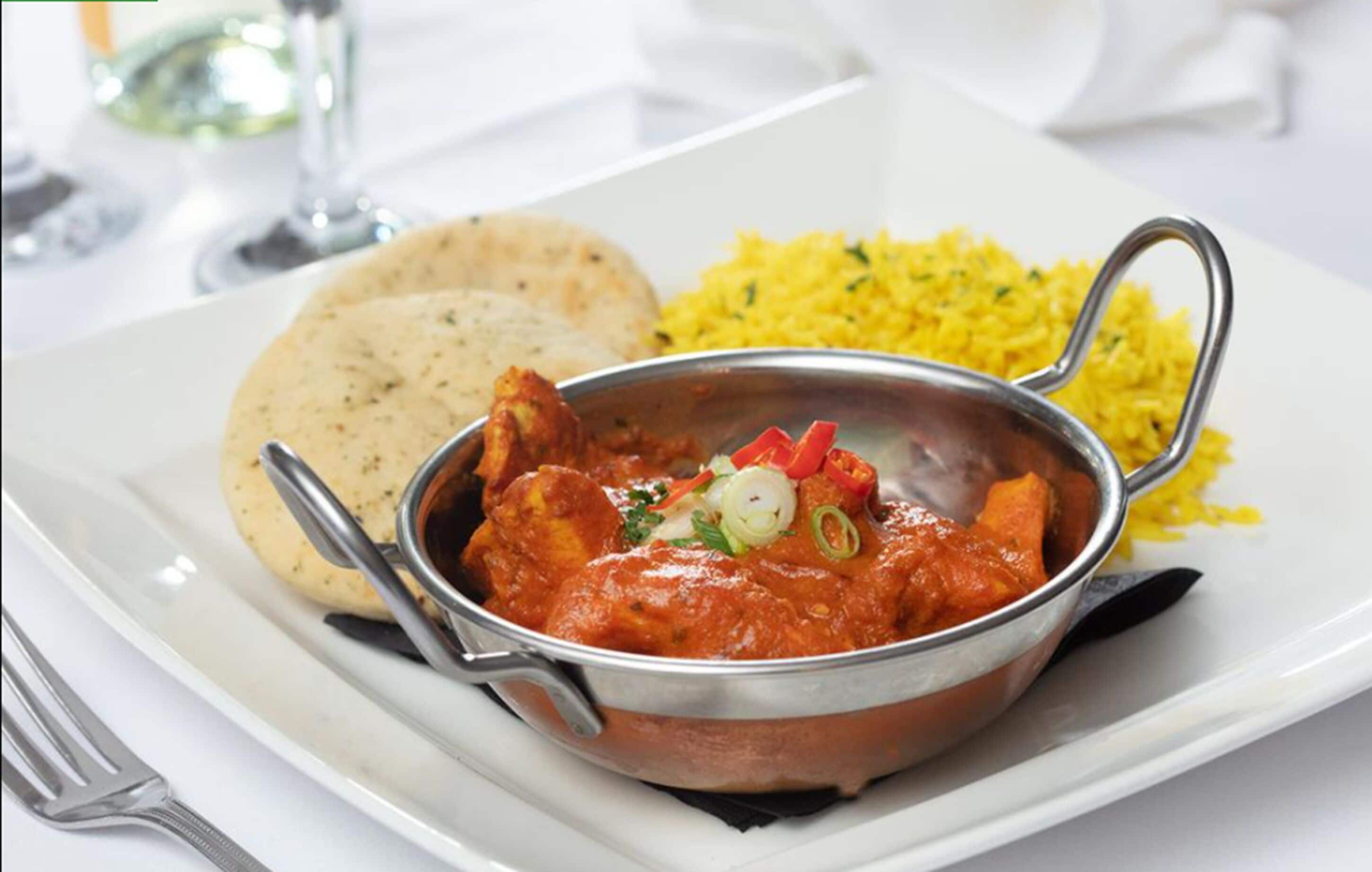 A meal consisting of a curry dish, yellow rice, and flatbread on a white plate.