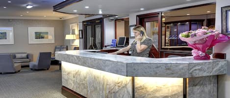 A hotel reception area with a marble counter, framed artwork on the walls, and a seating area with patterned sofas.