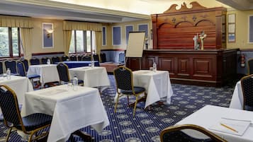 Un salón de conferencias con mesas, sillas, una pizarra y un panel de madera con detalles decorativos tallados.