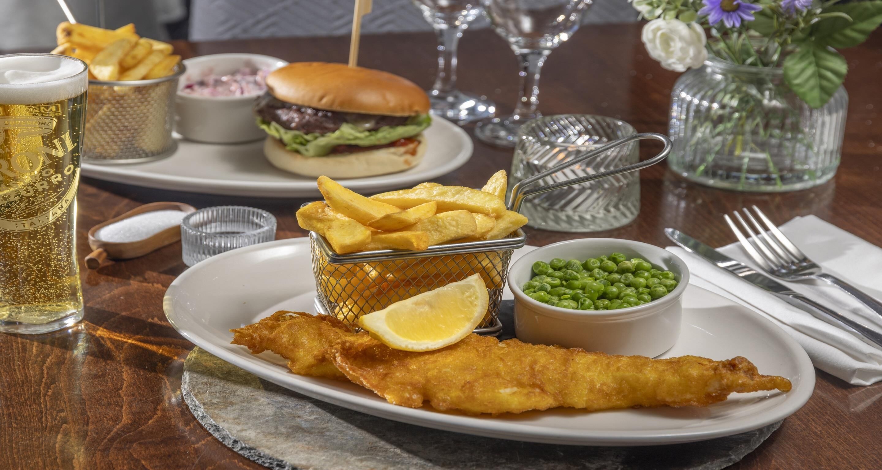 Un plato con un gran plato de pescado y papas fritas, una hamburguesa y una jarra de cerveza.