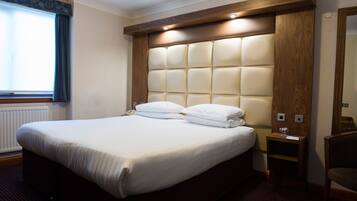 A hotel room with a large bed, a wooden headboard, a nightstand, and a chair.