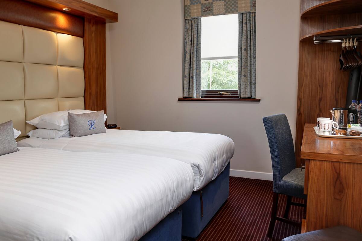 Une chambre d’hôtel avec un grand lit, un bureau avec une chaise et une fenêtre avec des rideaux.