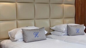 A hotel room with a tufted headboard, white bedding, and two pillows with a monogram.