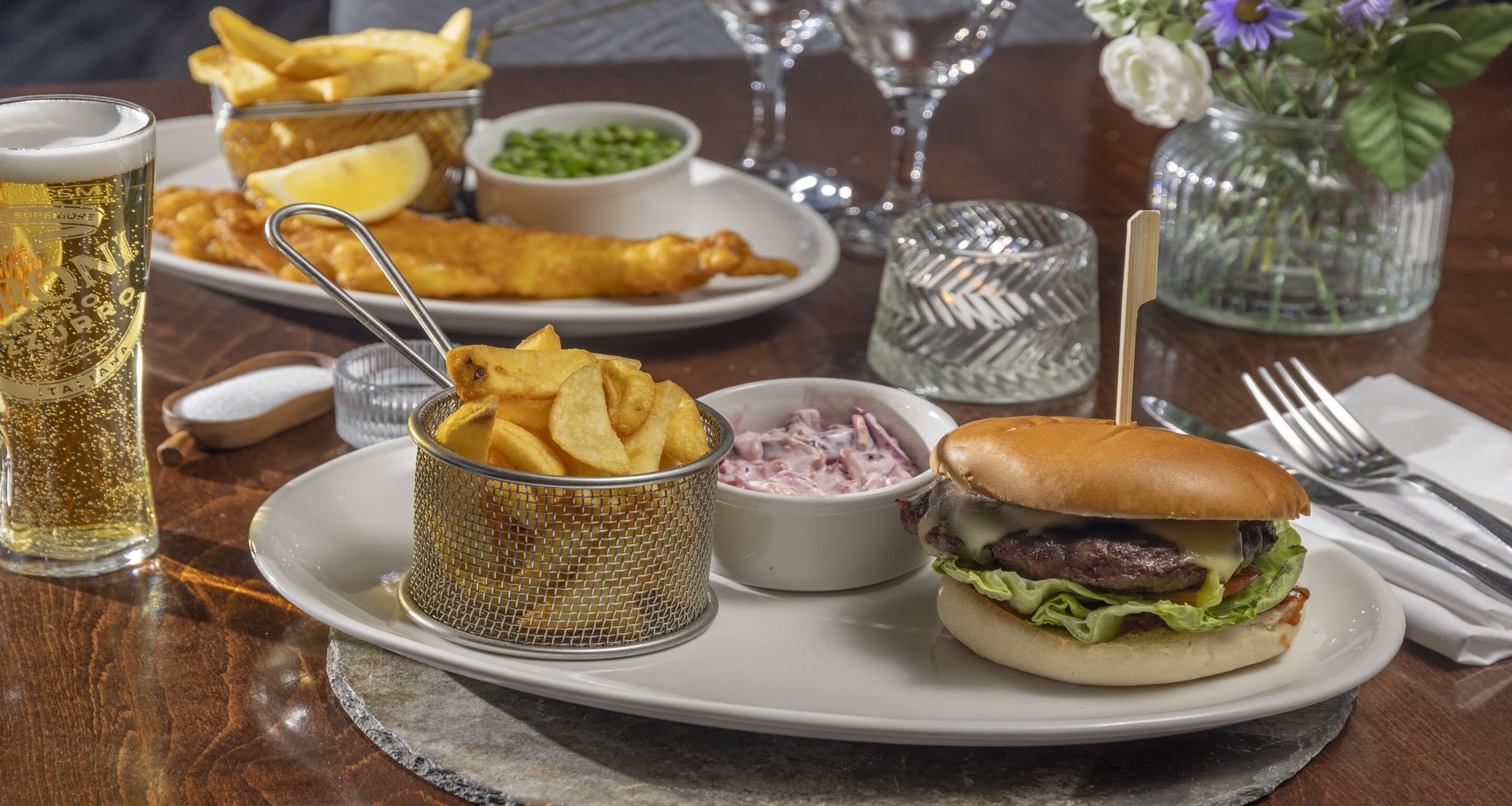 A meal with a burger, chips, and fish and chips, along with a beer and a glass of water on a table.