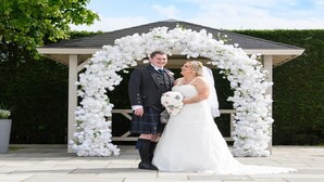A couple standing under a white floral archway.