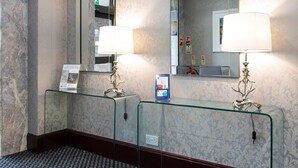 A hotel bathroom with marble walls, two glass-topped sinks, and wall-mounted mirrors.