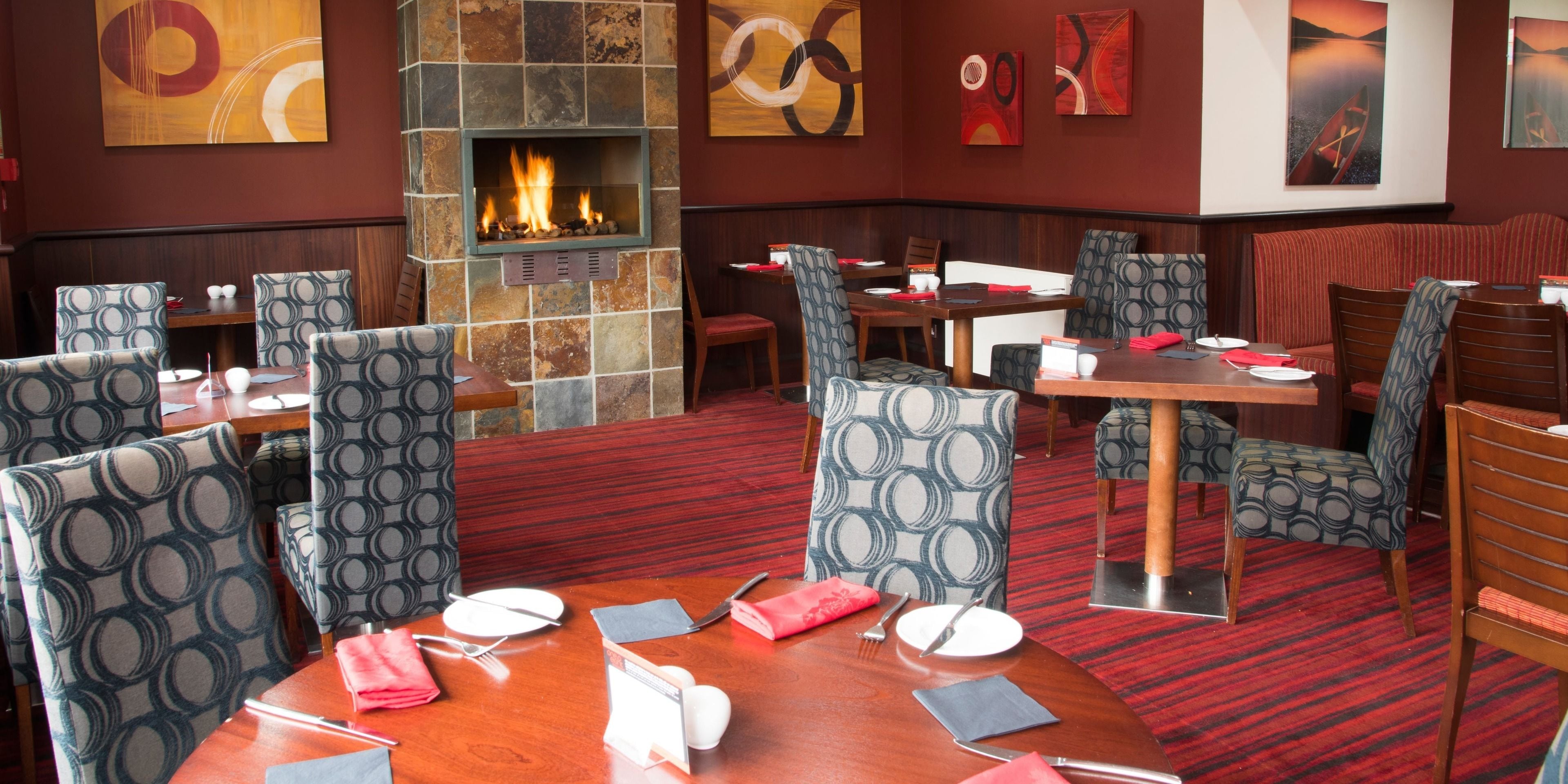 Un restaurante con chimenea de piedra, sillas estampadas y piso cubierto de alfombra roja.