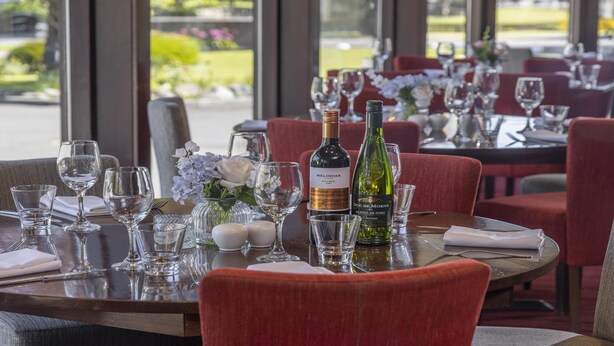 A restaurant table set with wine glasses, a bottle of wine, and a vase of flowers.