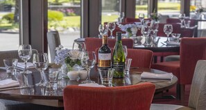 Une table de restaurant dressée avec des verres à vin, une bouteille de vin et un vase de fleurs.