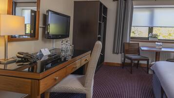 Habitación de hotel con escritorio, televisor, teléfono, una silla, cama y ventana con vista a árboles.