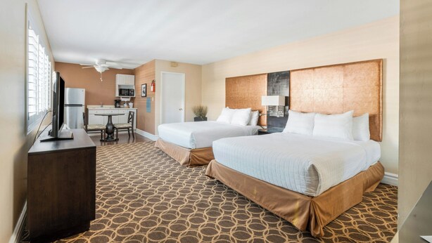 A hotel room with two beds, a desk, a chair, a television, and a ceiling fan. - Marin Suites Hotel (Corte Madera)