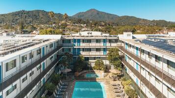 A multi-story hotel with a rooftop pool, balconies, and a view of a mountain.