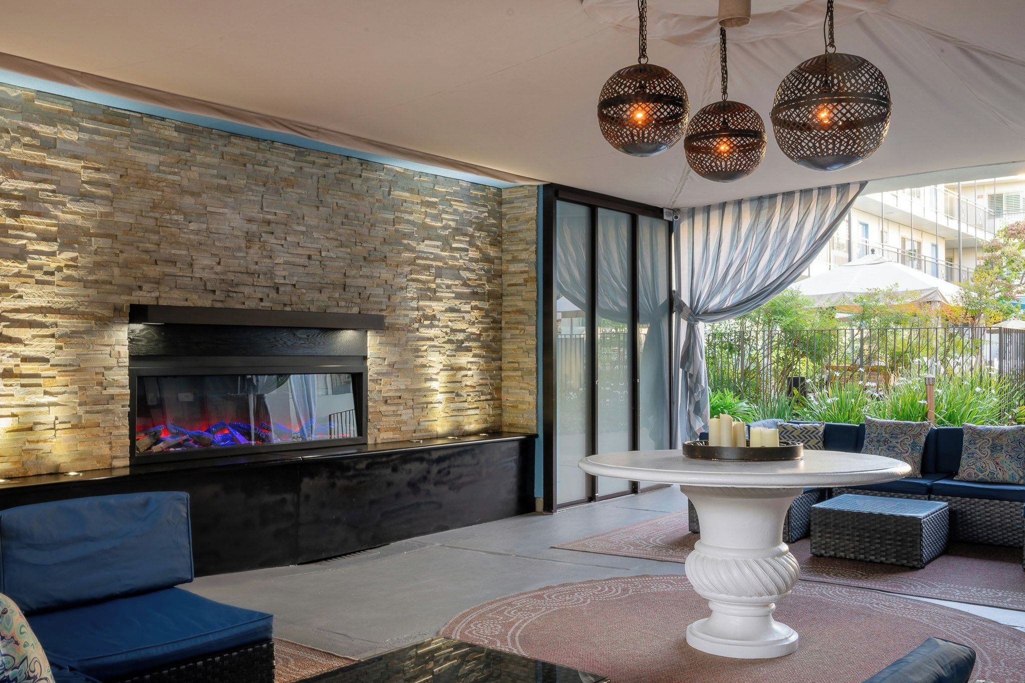 A modern outdoor seating area with a stone wall, a fireplace, and a dining table.