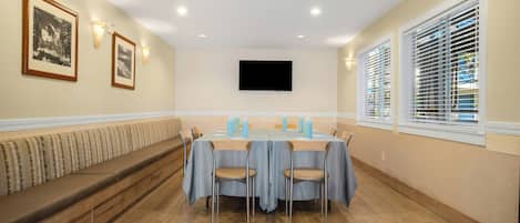 A conference room with a long table, chairs, a bench, and a flat-screen TV on the wall.