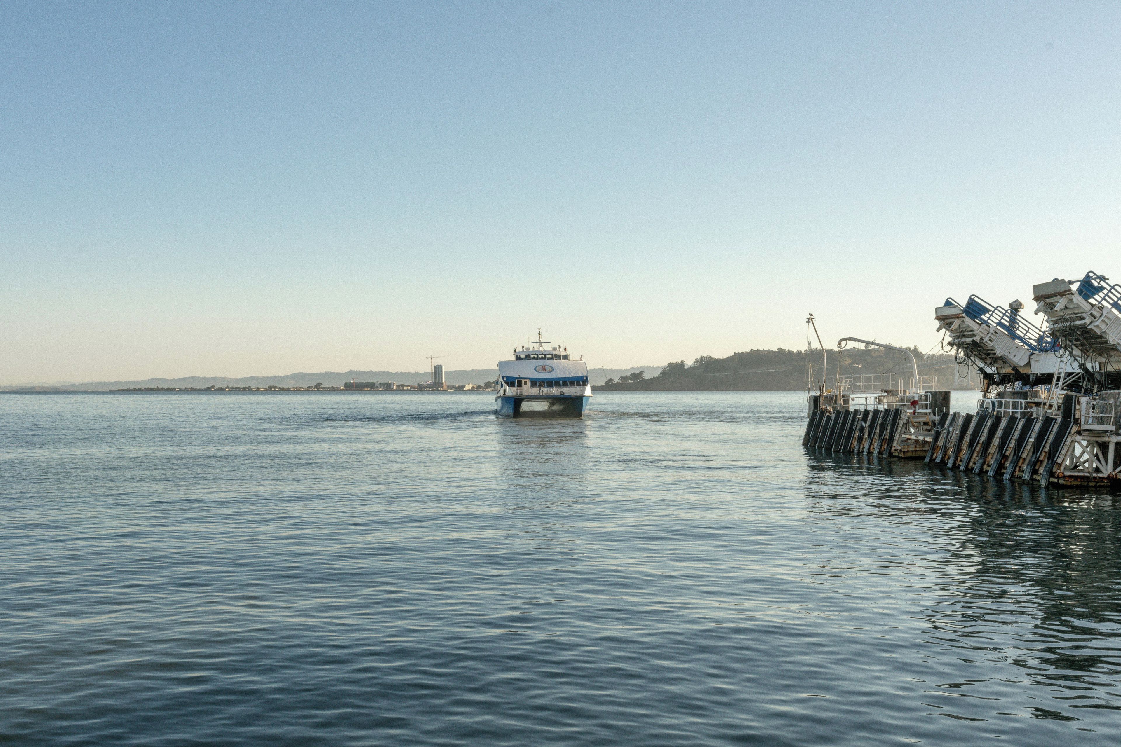 A ferry boat docked at a pier with a calm body of water and a clear sky.