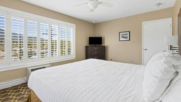 A bedroom with a bed, a ceiling fan, a dresser, a television, and a window with blinds.