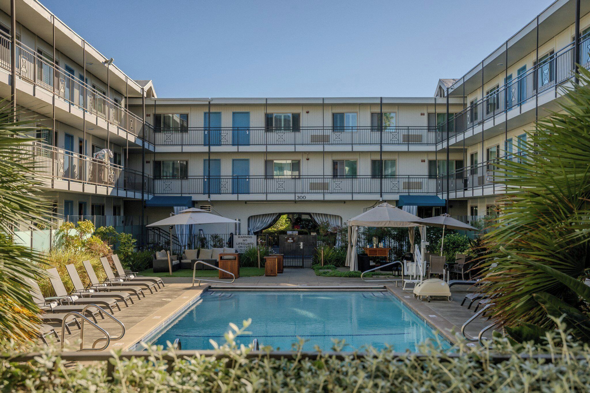 A pool area with lounge chairs, umbrellas, and a building with balconies.