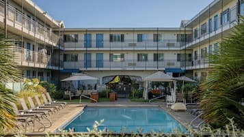 A pool area with lounge chairs, umbrellas, and a building with balconies.