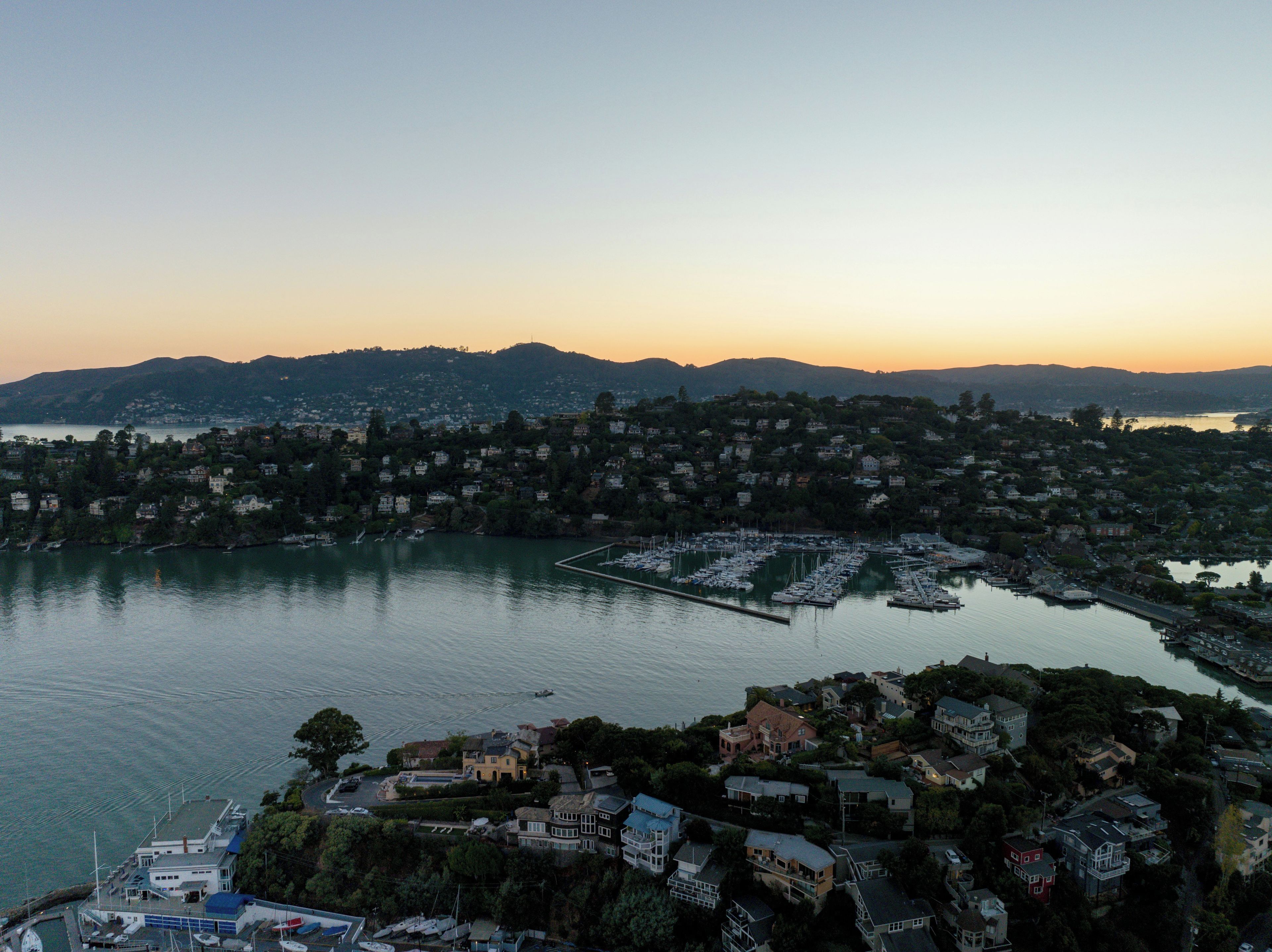 Uma cidade costeira com um porto de iates, edifícios residenciais e colinas ao fundo.