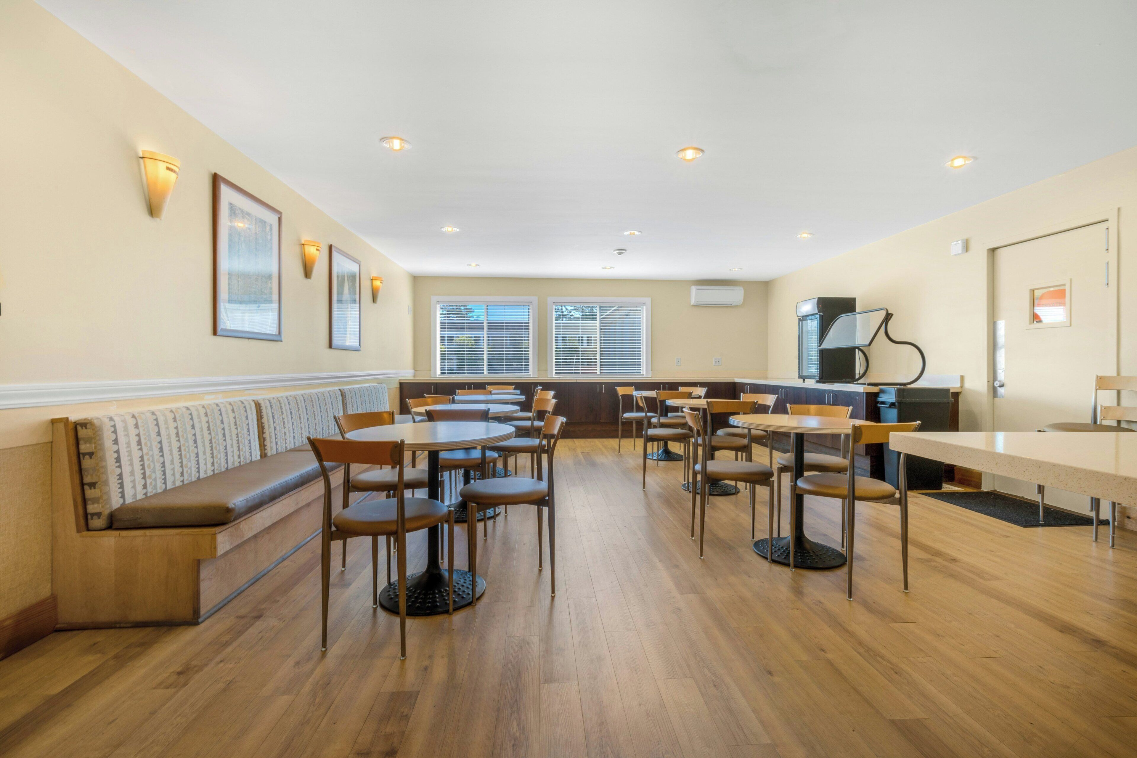 Ein Restaurant mit Holzboden, mehreren Tischen und Stühlen, einer Theke und einer Sitzgruppe mit einer Bank.
