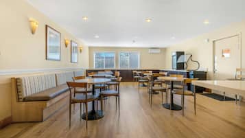 Un restaurante con suelo de madera, varias mesas y sillas, una barra y un área de estar con un banco.
