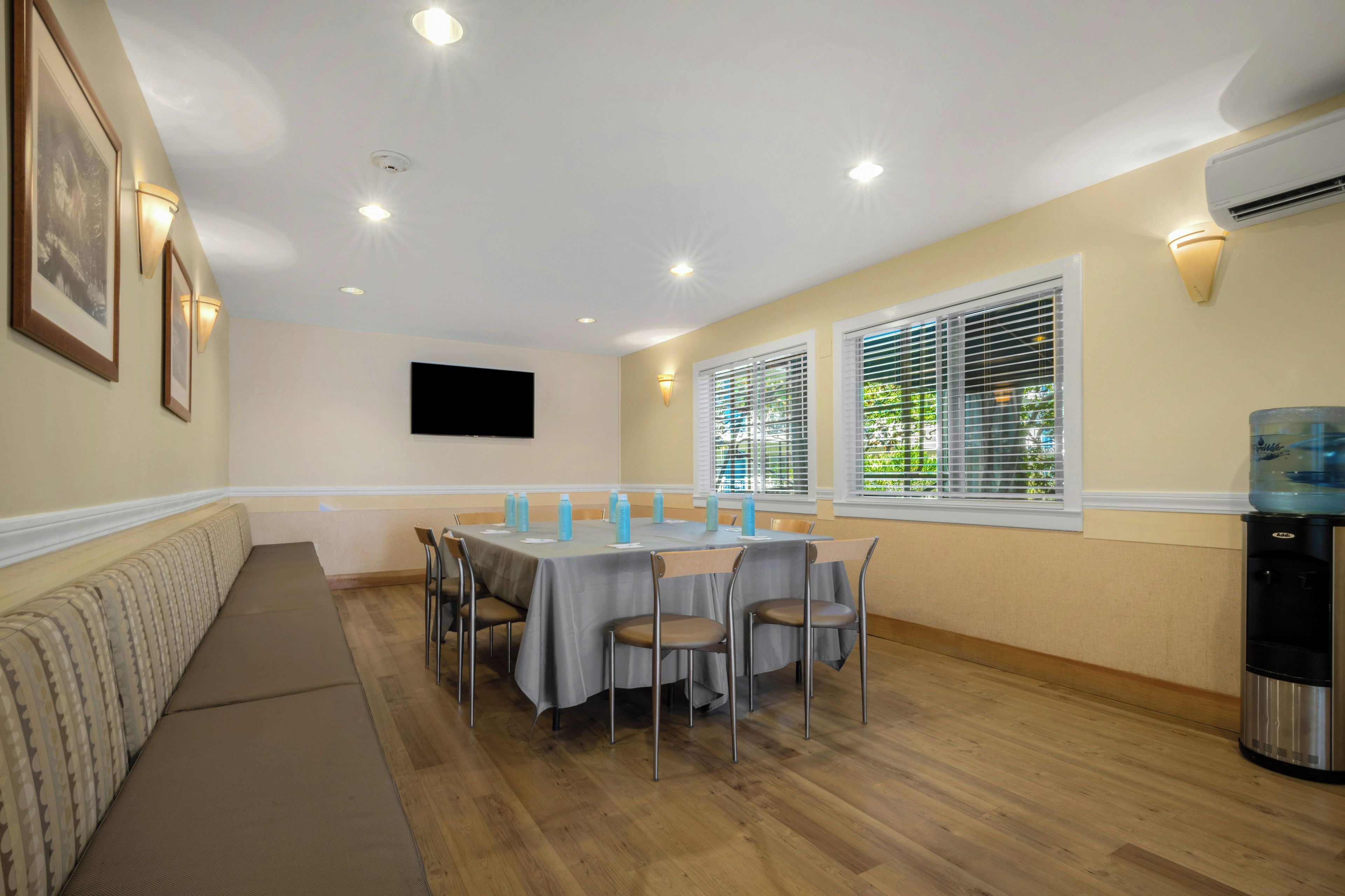 A dining area with a long table, chairs, a sofa, and a TV mounted on the wall.