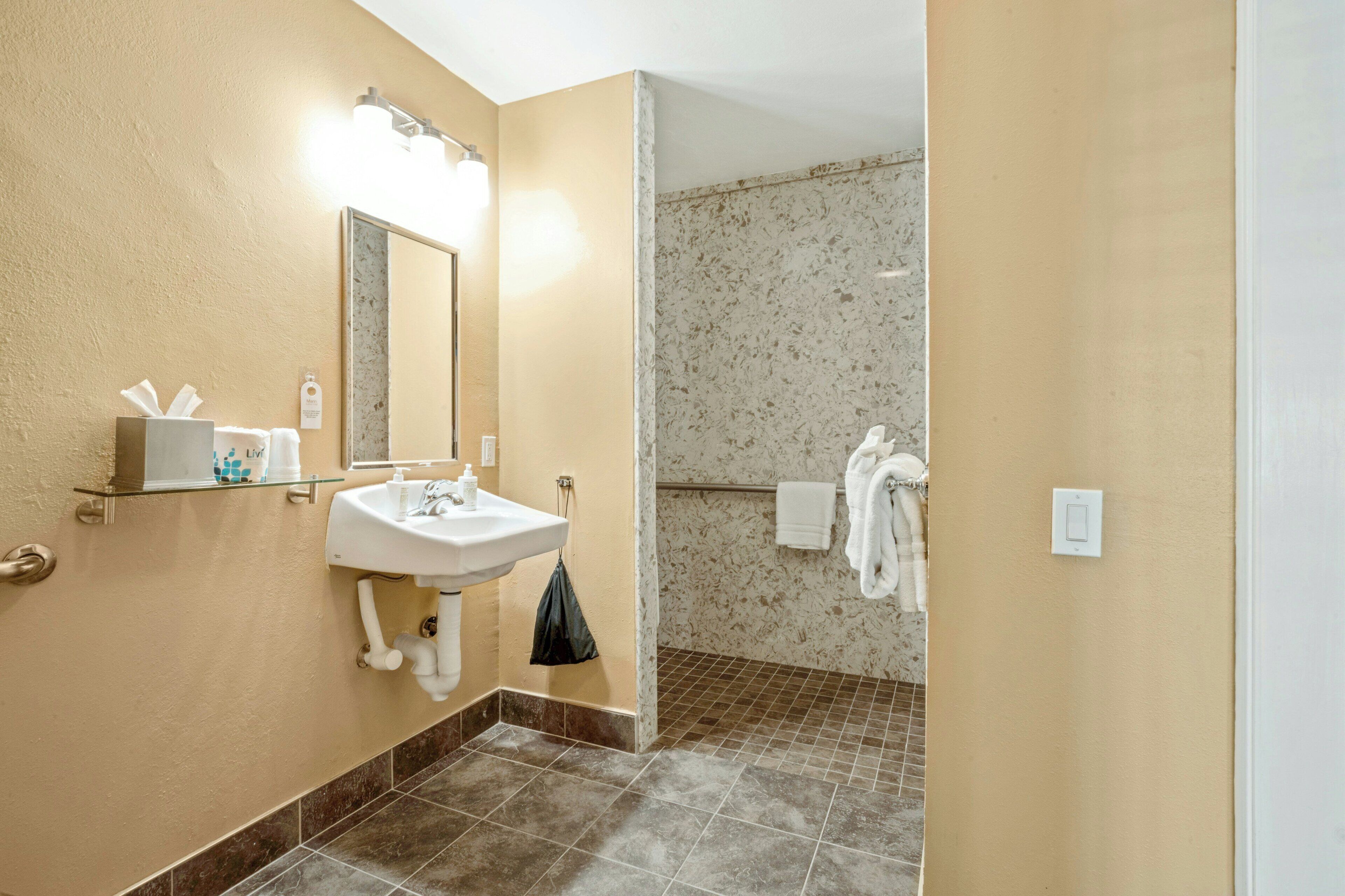 A bathroom with a sink, mirror, towel rack, and shower area.