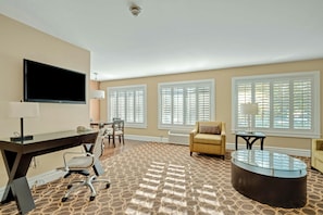 A hotel room with a flat-screen TV, a desk, a chair, a sofa, and a coffee table. - Marin Suites Hotel (Corte Madera)
